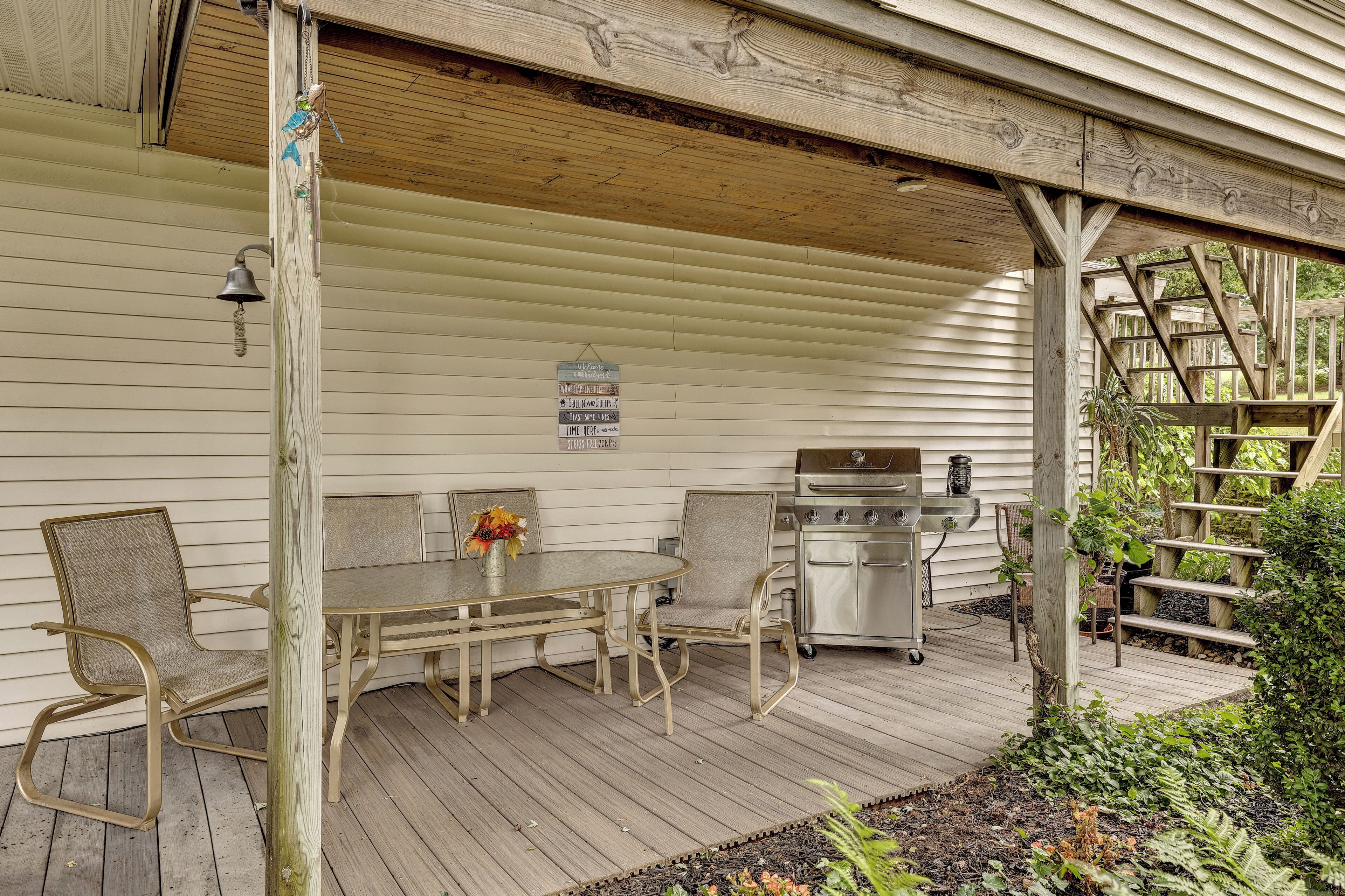 A covered outdoor patio with a table and chairs, a grill, and a signboard.