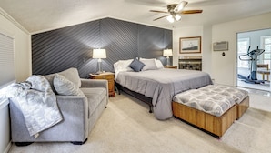 A bedroom with a bed, a sofa, a ceiling fan, a nightstand, a lamp, a picture frame, and a window. - Game Room, Deck + Yard! Cadillac Family Escape (Cadillac)