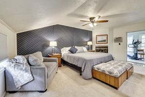 A bedroom with a bed, a sofa, a ceiling fan, a nightstand, a lamp, a picture frame, and a window. - Game Room, Deck + Yard! Cadillac Family Escape (Cadillac)