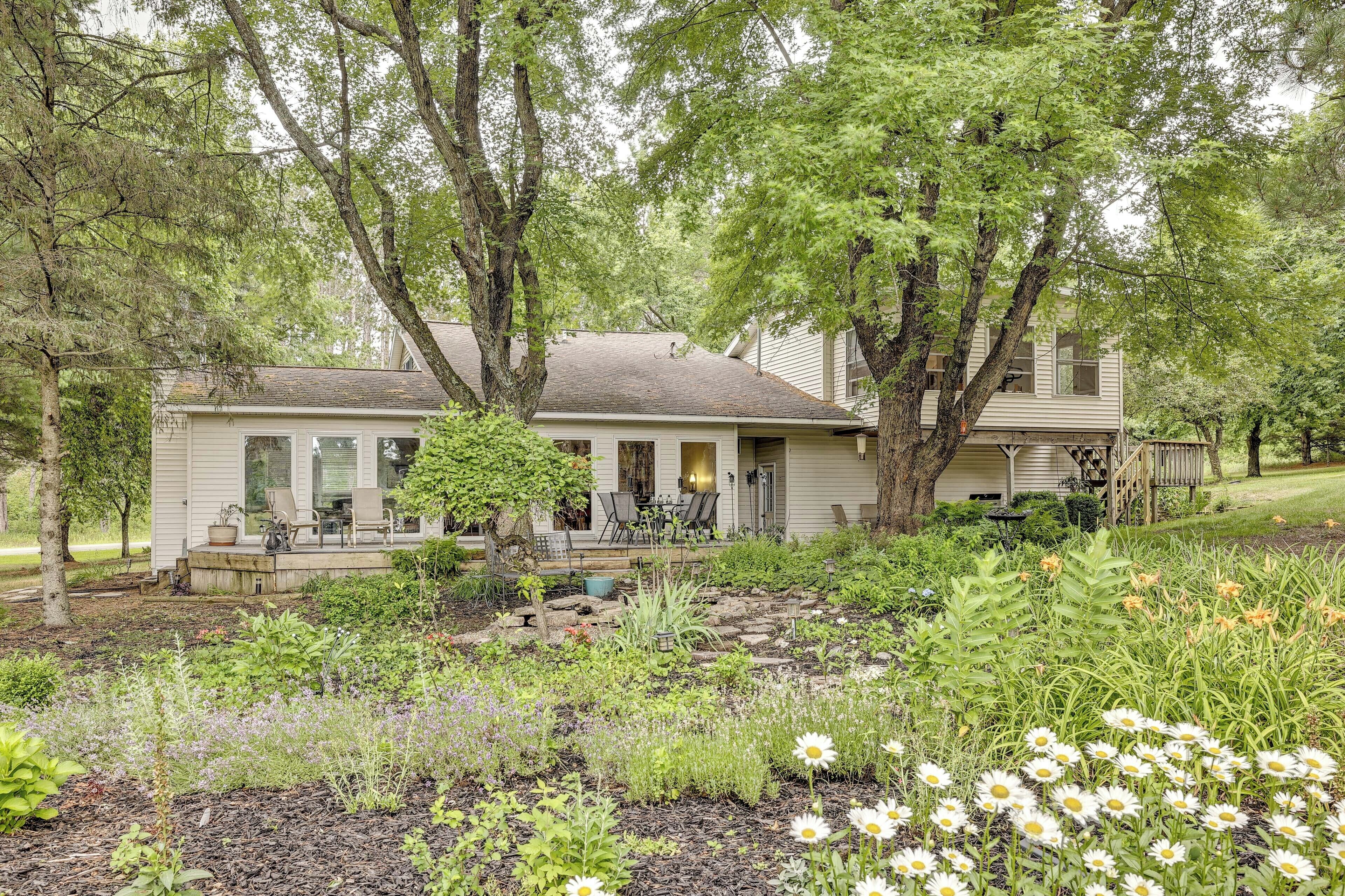 A two-story house with a covered porch, surrounded by a garden with various plants and flowers.