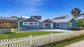 A two-story house with a front porch, a fenced yard, and a clear blue sky.