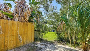A wooden deck leading to a grassy yard with a wooden fence and tropical plants. - Walk to the Sand! St Augustine Beach Bungalow (St. Augustine)