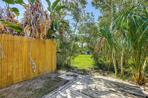 A wooden deck leading to a grassy yard with a wooden fence and tropical plants. - Walk to the Sand! St Augustine Beach Bungalow (St. Augustine)