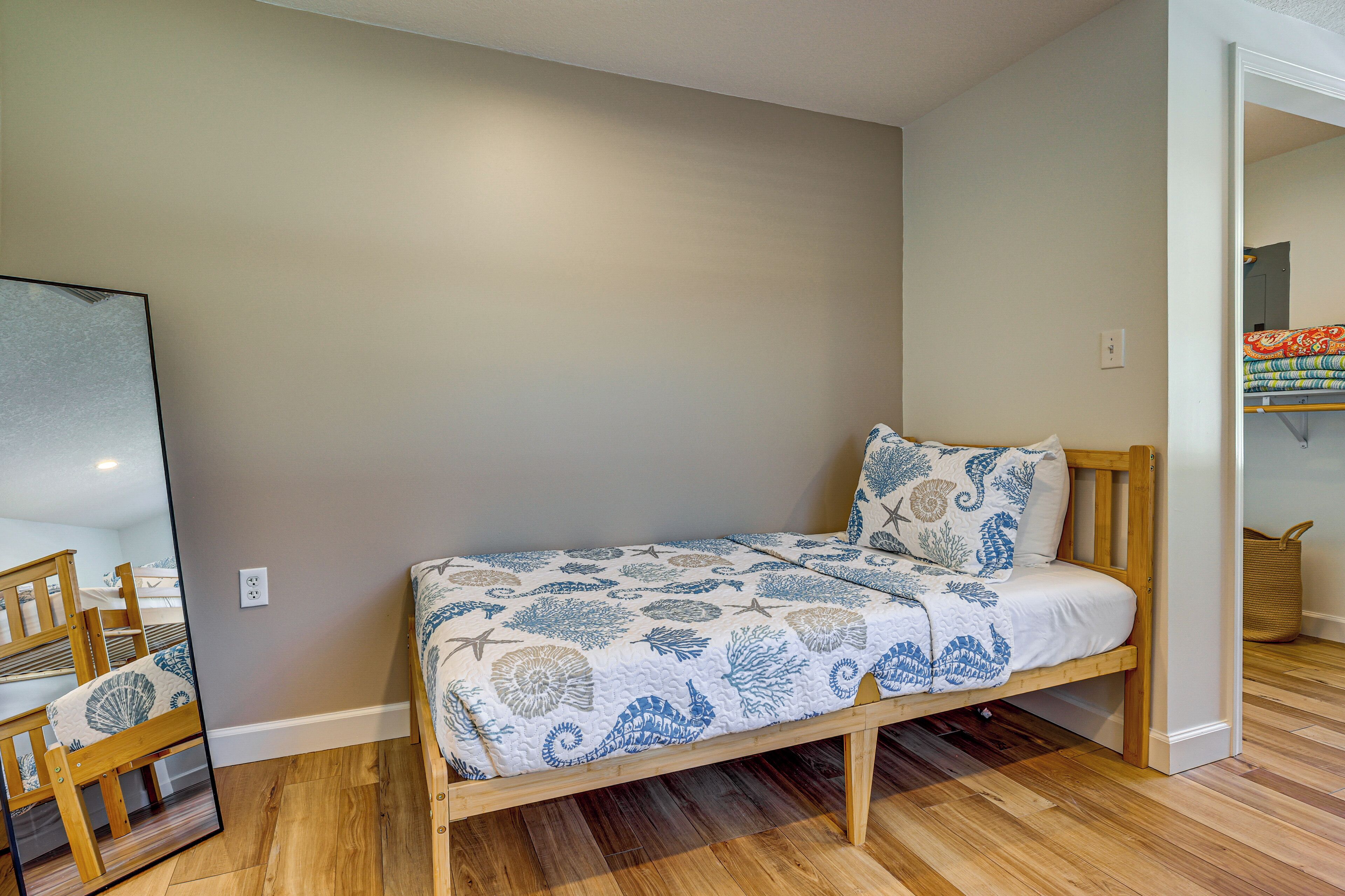 A single bed with a patterned bedspread and pillows, a wooden chair, and a mirror on the wall.