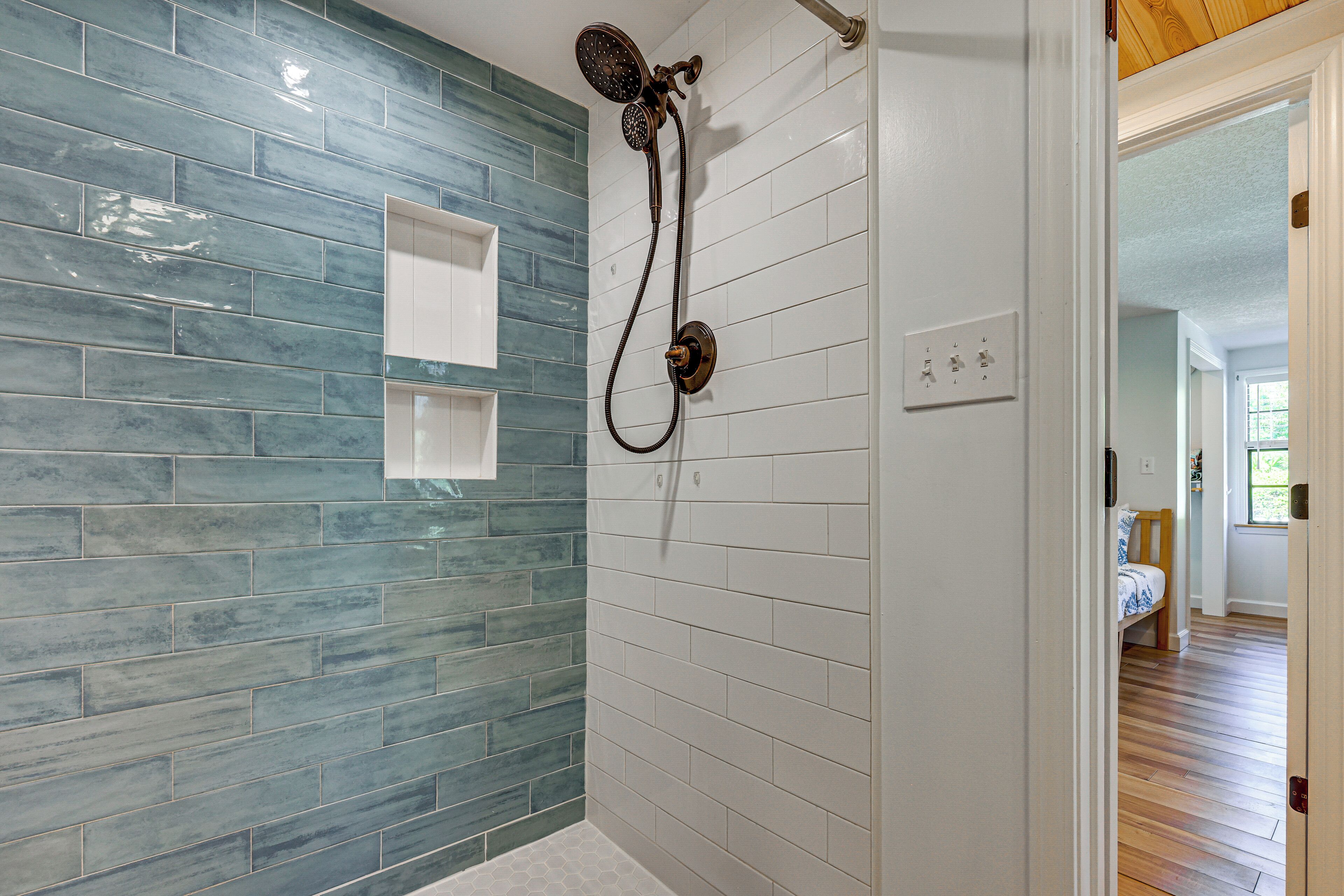 Une salle de bain avec une douche, des murs carrelés et une porte visible donnant sur une autre pièce.