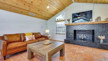 A living room with a brown leather sofa, a wooden coffee table, a black brick fireplace, and a ceiling fan.