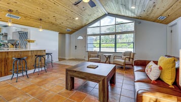 Un vaste espace de vie doté d’un plafond en bois, d’une table à manger, d’un canapé et d’un coin cuisine avec des tabourets de bar.