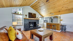 A living room with a fireplace, a sofa, a coffee table, and a kitchen area with bar stools. - Walk to the Sand! St Augustine Beach Bungalow (St. Augustine)