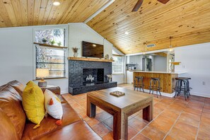 A living room with a fireplace, a sofa, a coffee table, and a kitchen area with bar stools. - Walk to the Sand! St Augustine Beach Bungalow (St. Augustine)