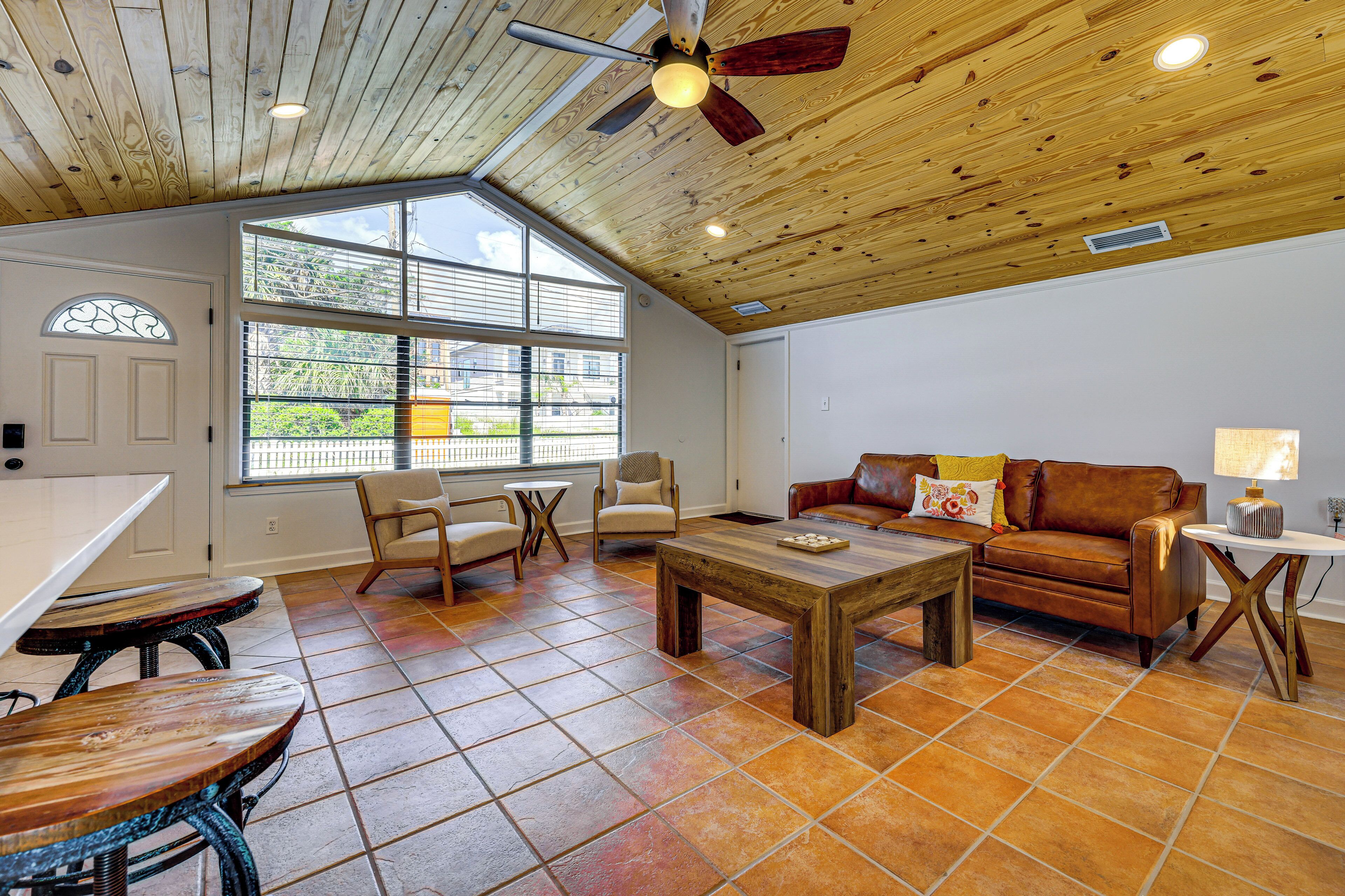 A spacious living area with a wooden ceiling, a large window, a brown leather sofa, and a round coffee table.