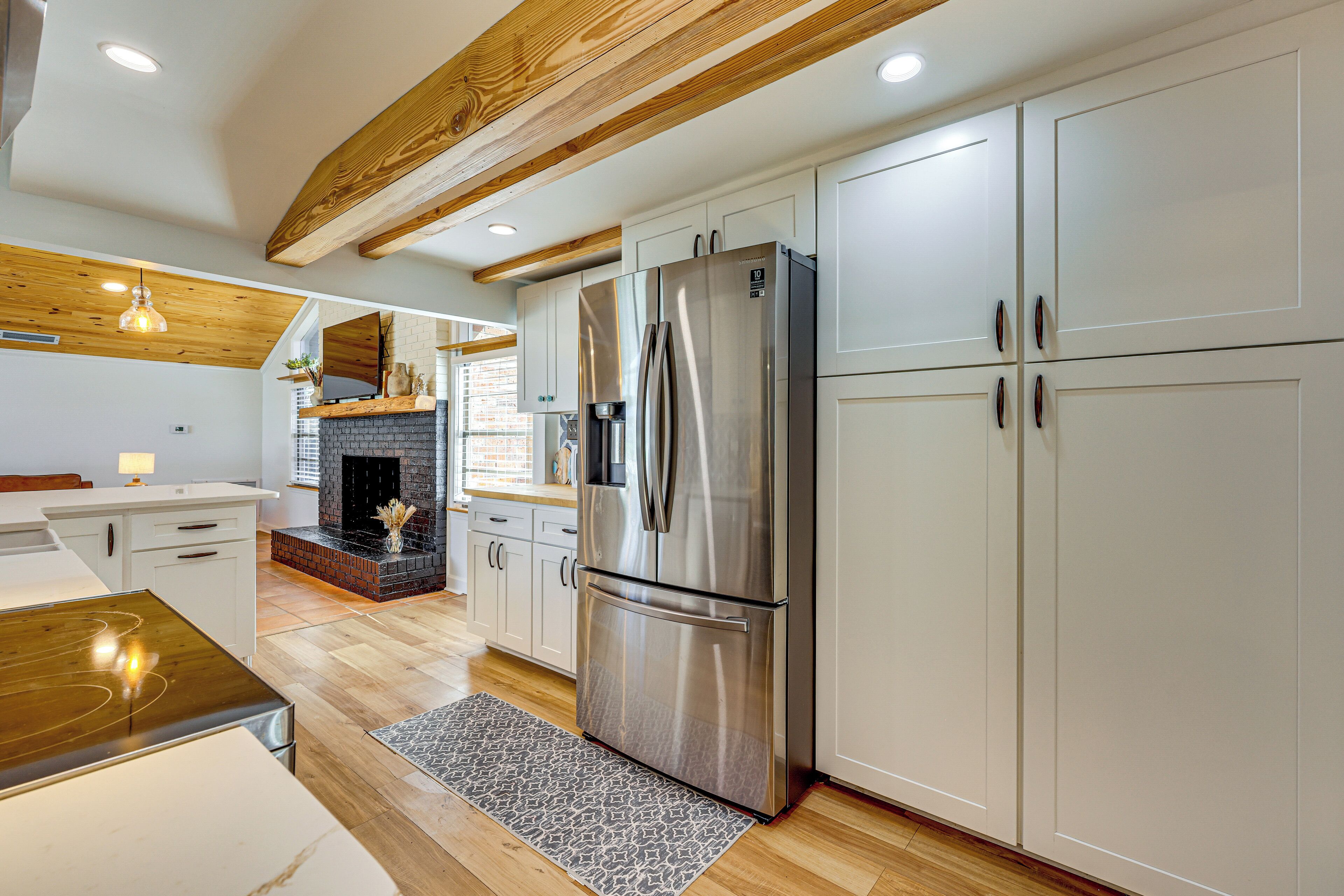 A modern kitchen with white cabinetry, a stainless steel refrigerator, and a brick fireplace.