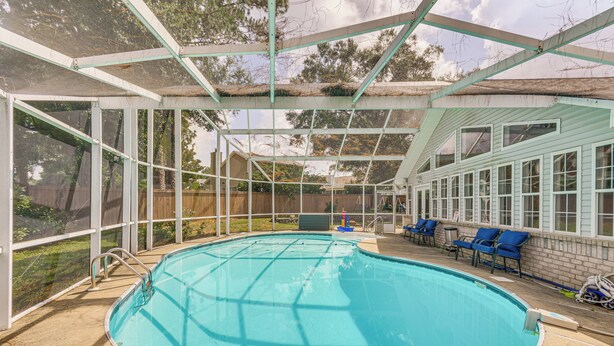 Una piscina techada con techo transparente, rodeada por una valla de madera, equipada con sillones de descanso y un calentador.