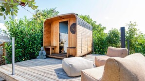 Een houten chalet met een deur, een klein tafeltje en twee rieten stoelen op een houten terras.