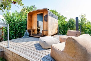 Uma cabana de madeira com porta, uma mesa pequena e duas cadeiras de vime em um deck de madeira.