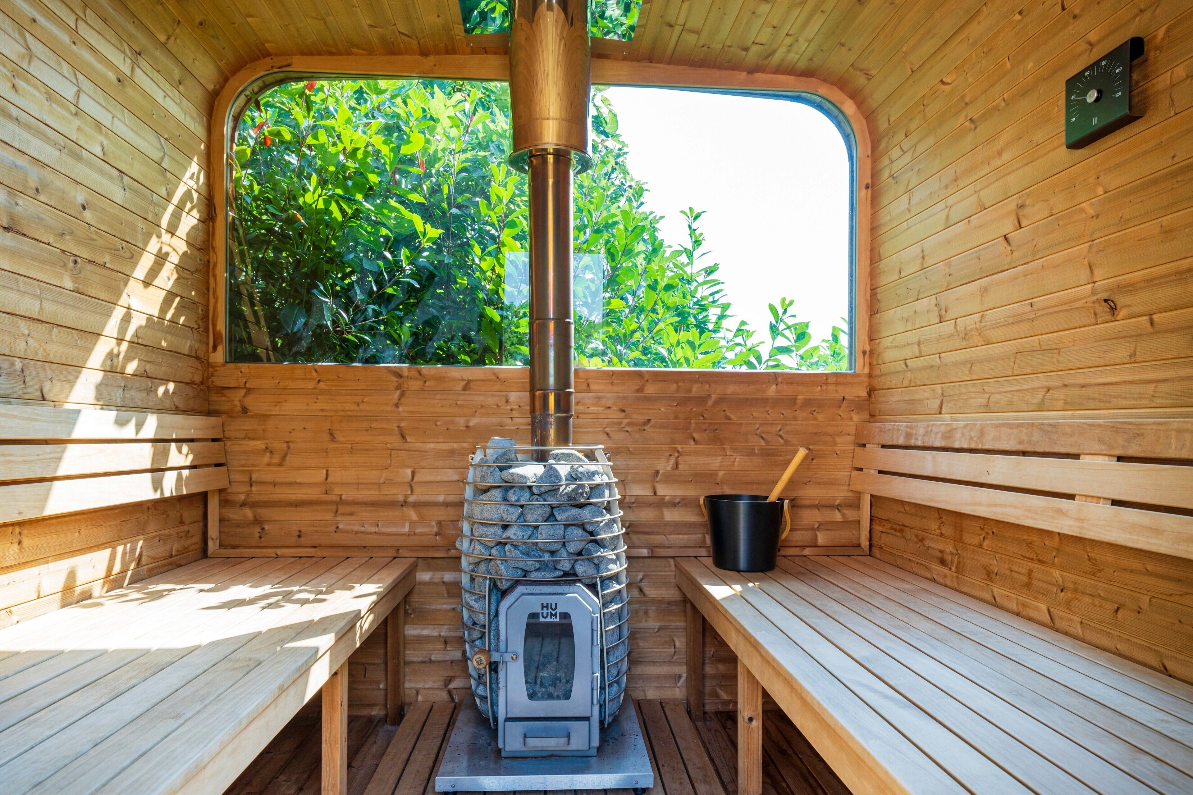 A sauna with wooden benches, a stone stove, and a window with a view of greenery.