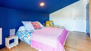 Een slaapkamer met een bed, nachtkastje, lamp en een stoel.