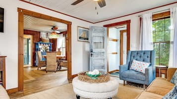 A cozy living room with a wooden ceiling, a dining area with wicker furniture, and a large window with curtains.