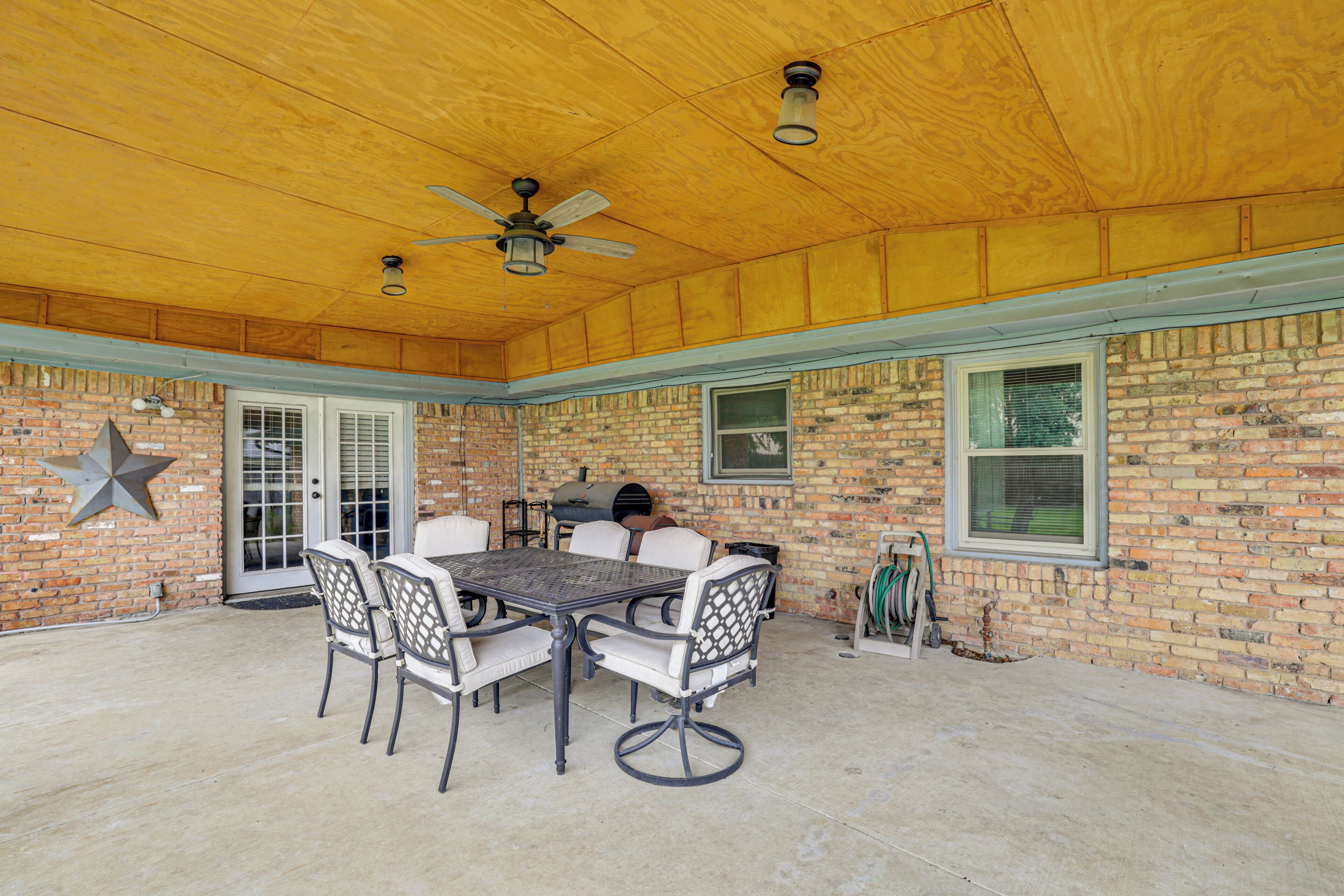 An outdoor patio with a brick wall, a ceiling fan, and a table with chairs.
