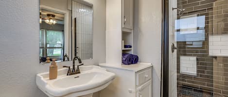 A bathroom with a white sink, a mirror, and a shower area with a glass door.