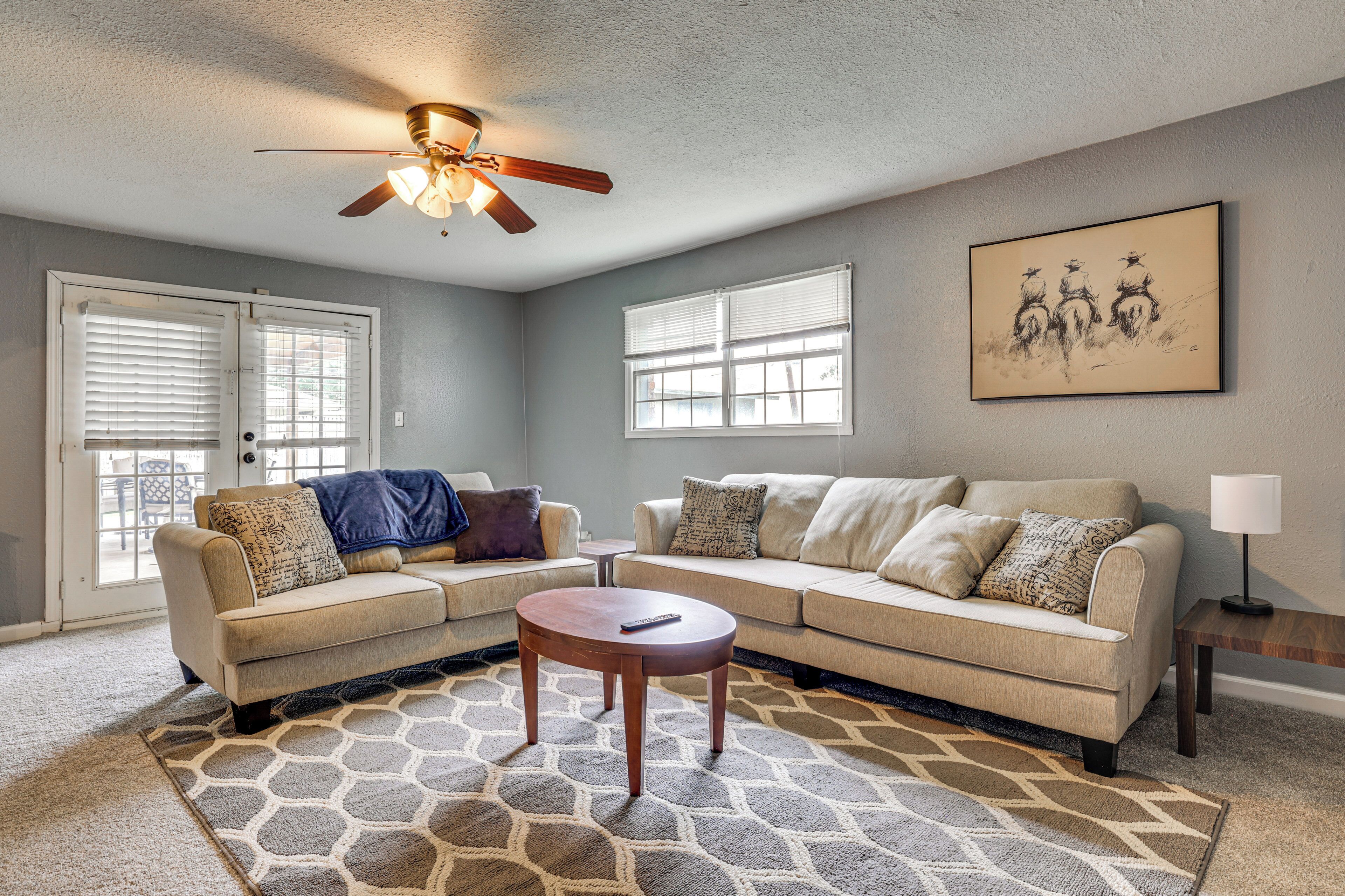 A living room with a beige sectional sofa, a round coffee table, a ceiling fan, and a painting on the wall.