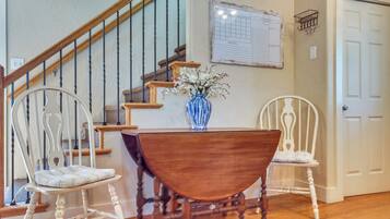 A staircase with a wooden handrail and metal balusters, a dining table with a vase of flowers, and two white upholstered chairs.