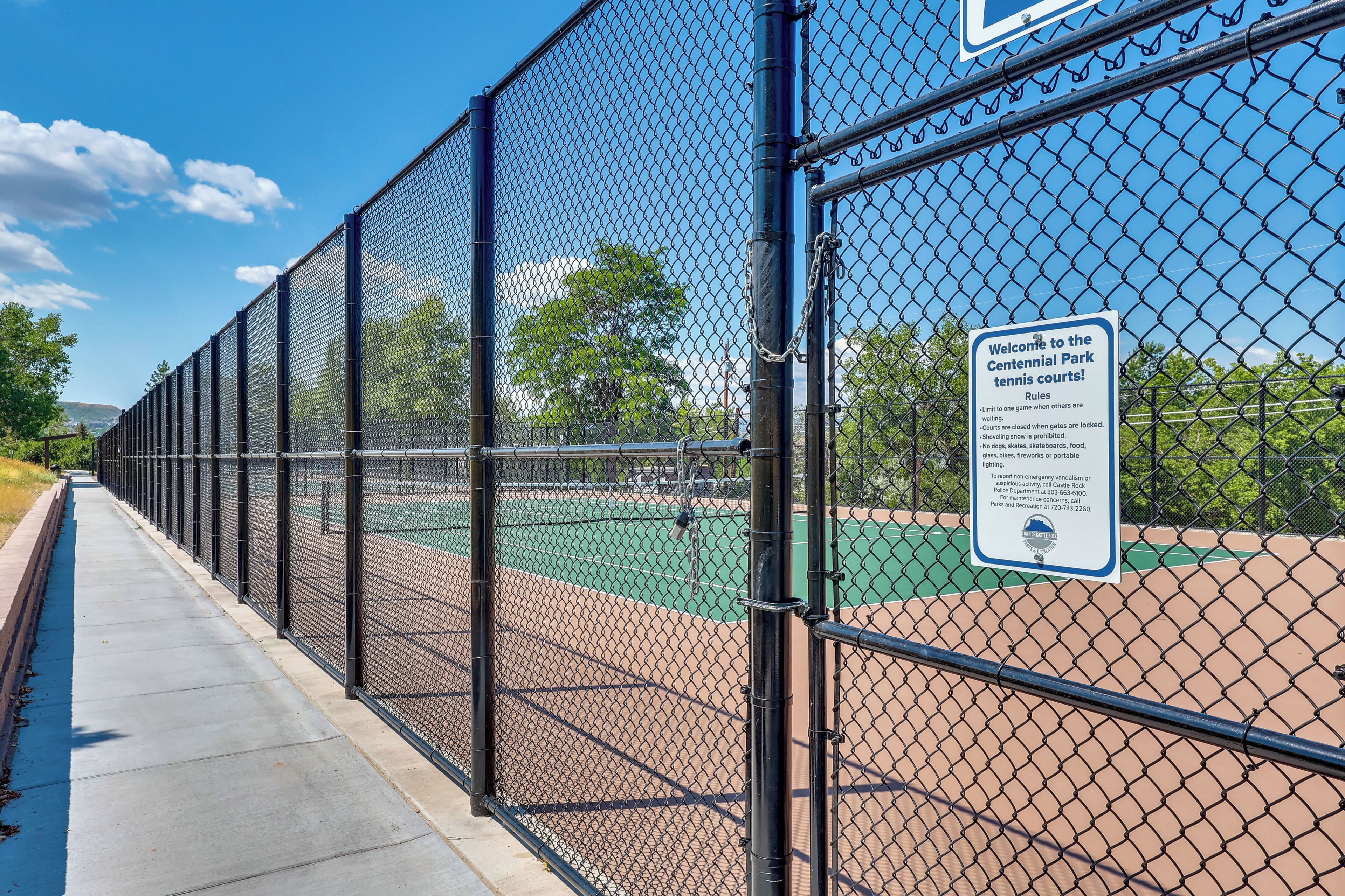 A chain-link fence surrounding a tennis court with a sign indicating rules and contact information for Castle Rock Police Department.