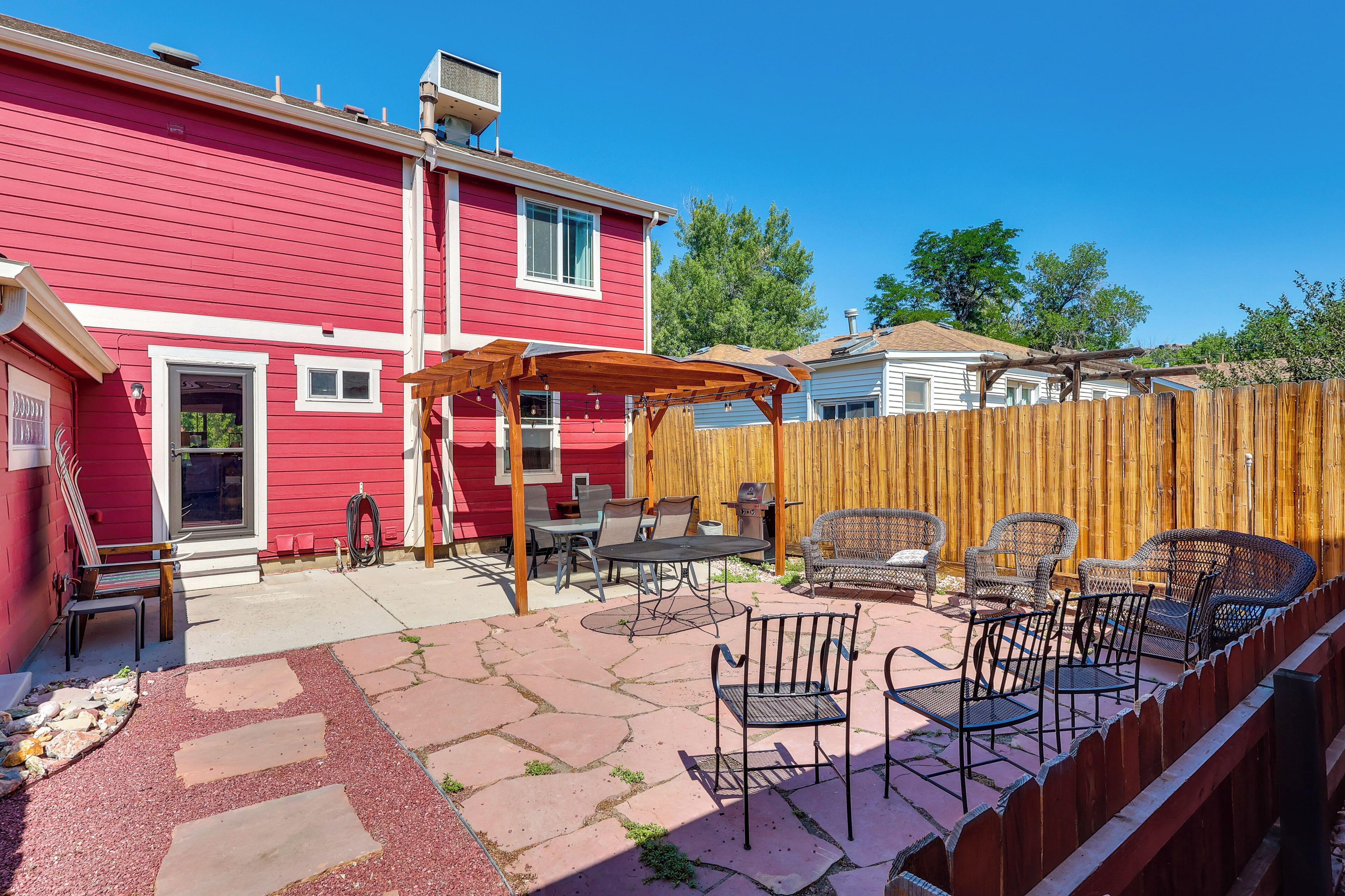 A red house with a patio area featuring outdoor furniture and a wooden pergola.