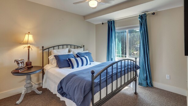 A bedroom with a bed, a nightstand, a lamp, a ceiling fan, and a window with curtains. - Historic Downtown Castle Rock Home (Castle Rock)