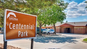A sign for Centennial Park in Castle Rock, Colorado, with a brick building and parked cars in the background. - Historic Downtown Castle Rock Home (Castle Rock)