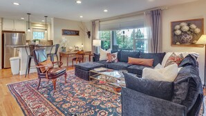 A spacious living room with a sofa, armchairs, a coffee table, and a rug. There is a kitchen area with cabinets and a refrigerator. - Historic Downtown Castle Rock Home (Castle Rock)