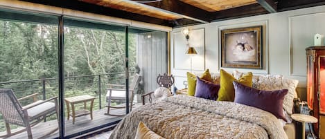 A bedroom with a large bed, a view of the outdoors, and a balcony with furniture.