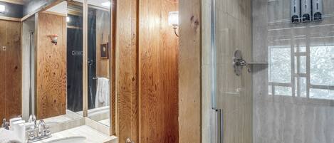 A bathroom with a wooden vanity, a large mirror, a glass shower enclosure, and a toilet paper holder.