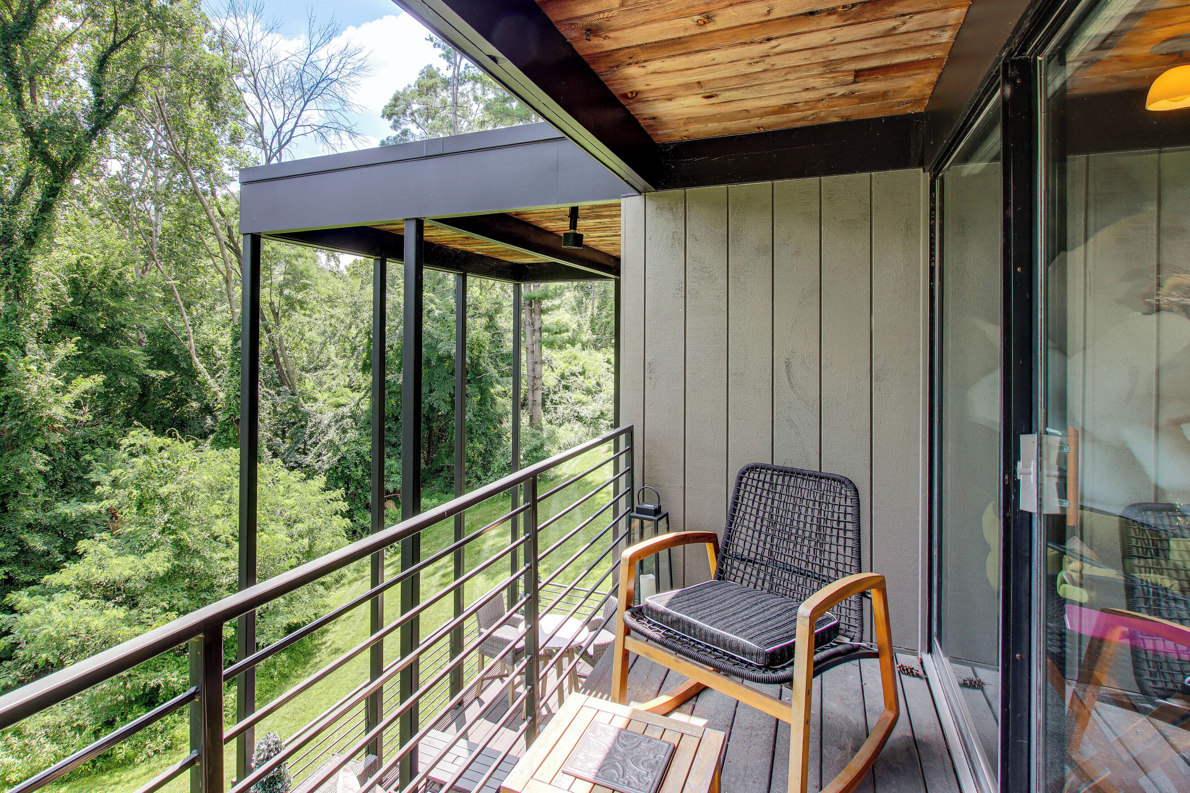 A balcony with a chair, a table, and a view of a forest.
