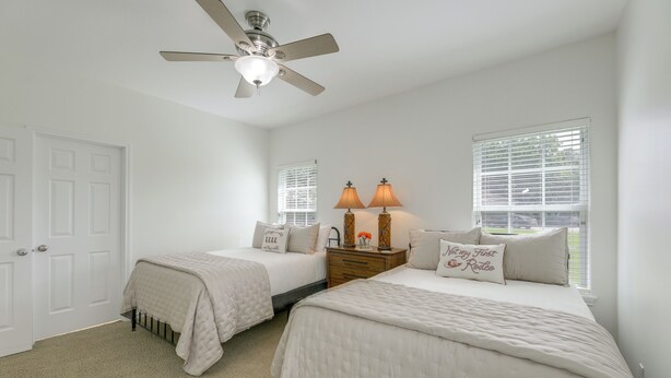 A bedroom with two beds, a ceiling fan, a nightstand with lamps, and a window with blinds. - On 174 Acres! Ranch House in Colorado County (Weimar)