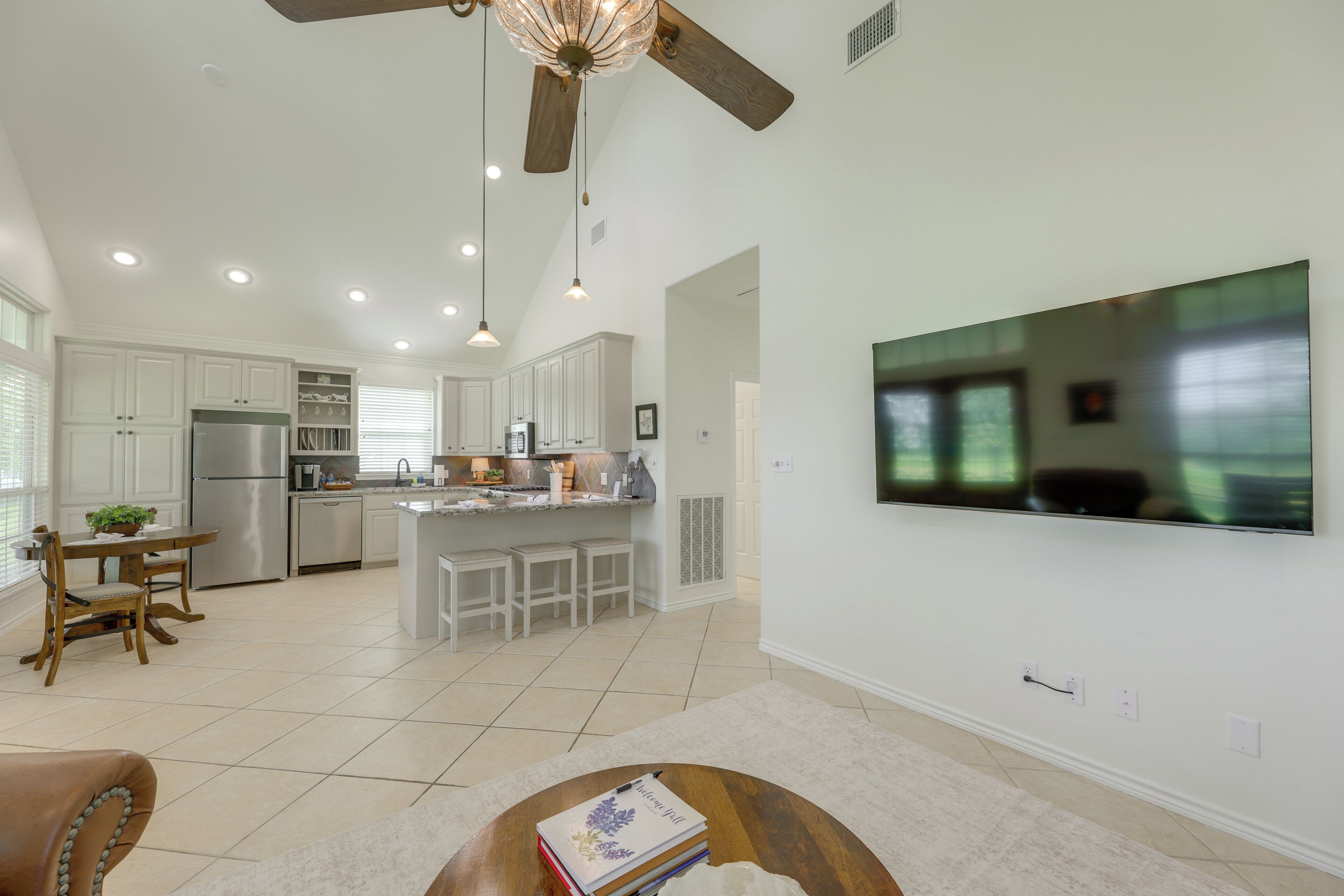 A spacious kitchen with a dining area, a ceiling fan, recessed lighting, and a large flat-screen TV mounted on the wall.