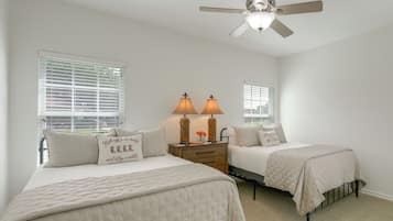 A bedroom with two beds, a ceiling fan, and a nightstand with lamps.