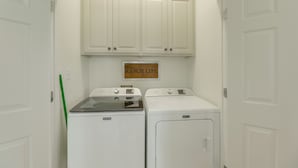 A laundry room with two Maytag washers and dryers, white cabinets above, and a 'RANCH LIFE' sign on the wall. - On 174 Acres! Ranch House in Colorado County (Weimar)
