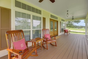 A covered porch with wooden rocking chairs and a bench, large windows, and a view of a green landscape. - On 174 Acres! Ranch House in Colorado County (Weimar)