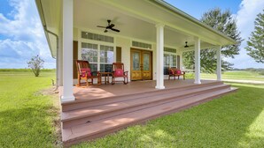 A covered porch with wooden chairs and a bench, a wooden door, and a view of a green landscape. - On 174 Acres! Ranch House in Colorado County (Weimar)