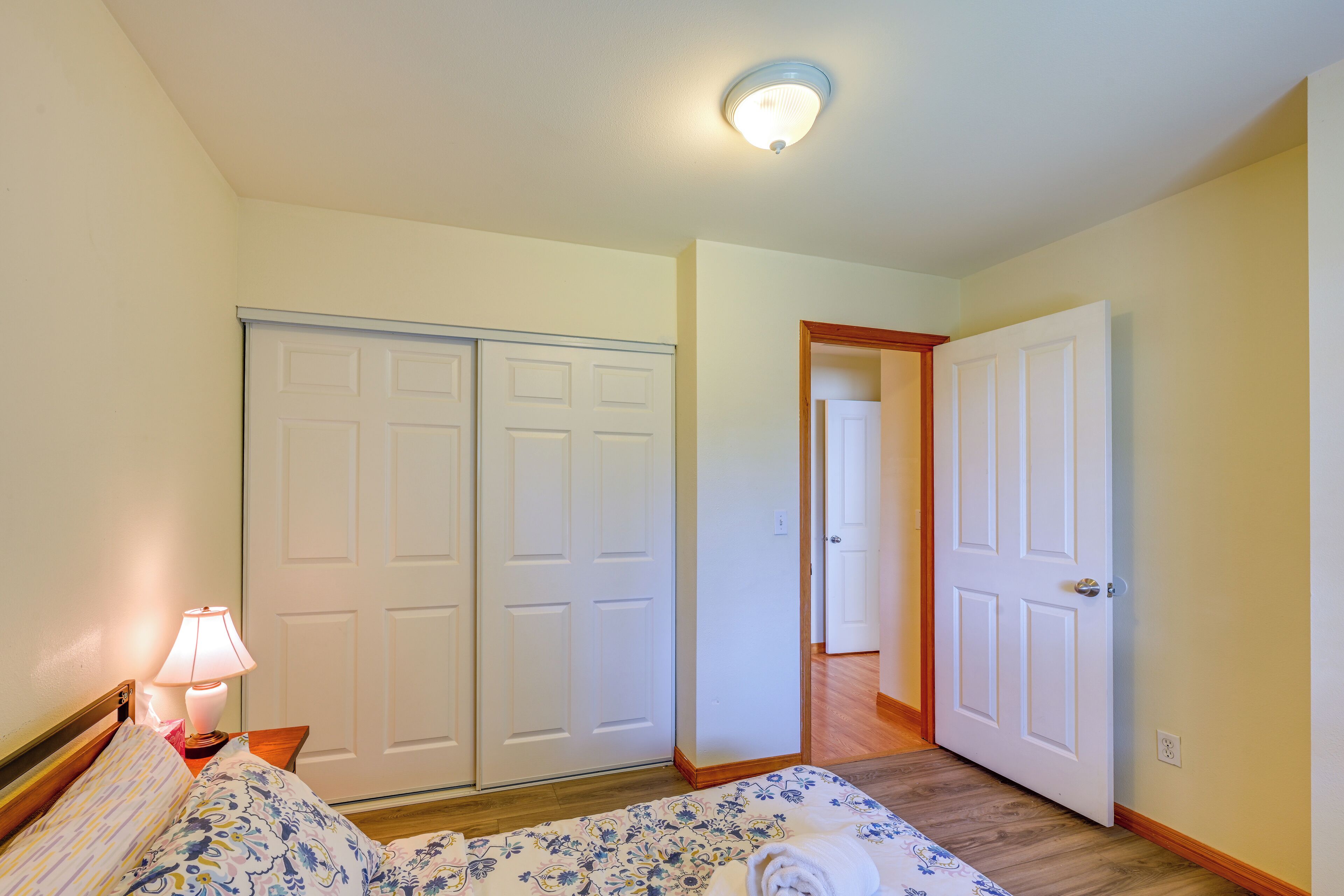 Une chambre à coucher comprenant un lit, une table de chevet, une lampe, une armoire et une porte donnant sur une autre pièce.
