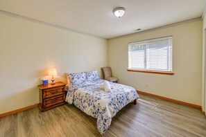 A bedroom with a bed, nightstand, lamp, chair, window with blinds, and wooden flooring.
