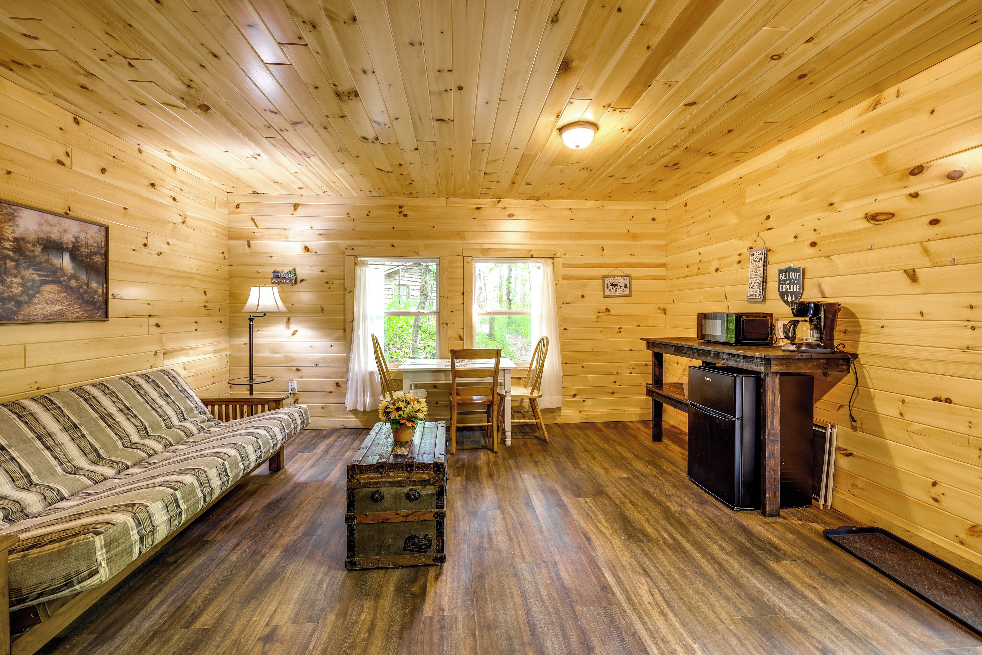 A cabin interior with a sofa, dining table, chairs, a small kitchen area, and a window.