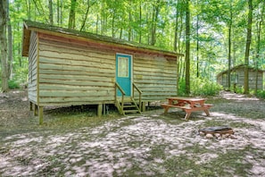 A rustic cabin with a door, a small porch, and a picnic table. - Cabin w/ Lake Access at Letchworth Valley Resort (Bliss)