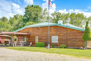 A rustic wooden cabin with a green roof, a flagpole with an American flag, and a small porch with outdoor seating. - Cabin w/ Lake Access at Letchworth Valley Resort (Bliss)
