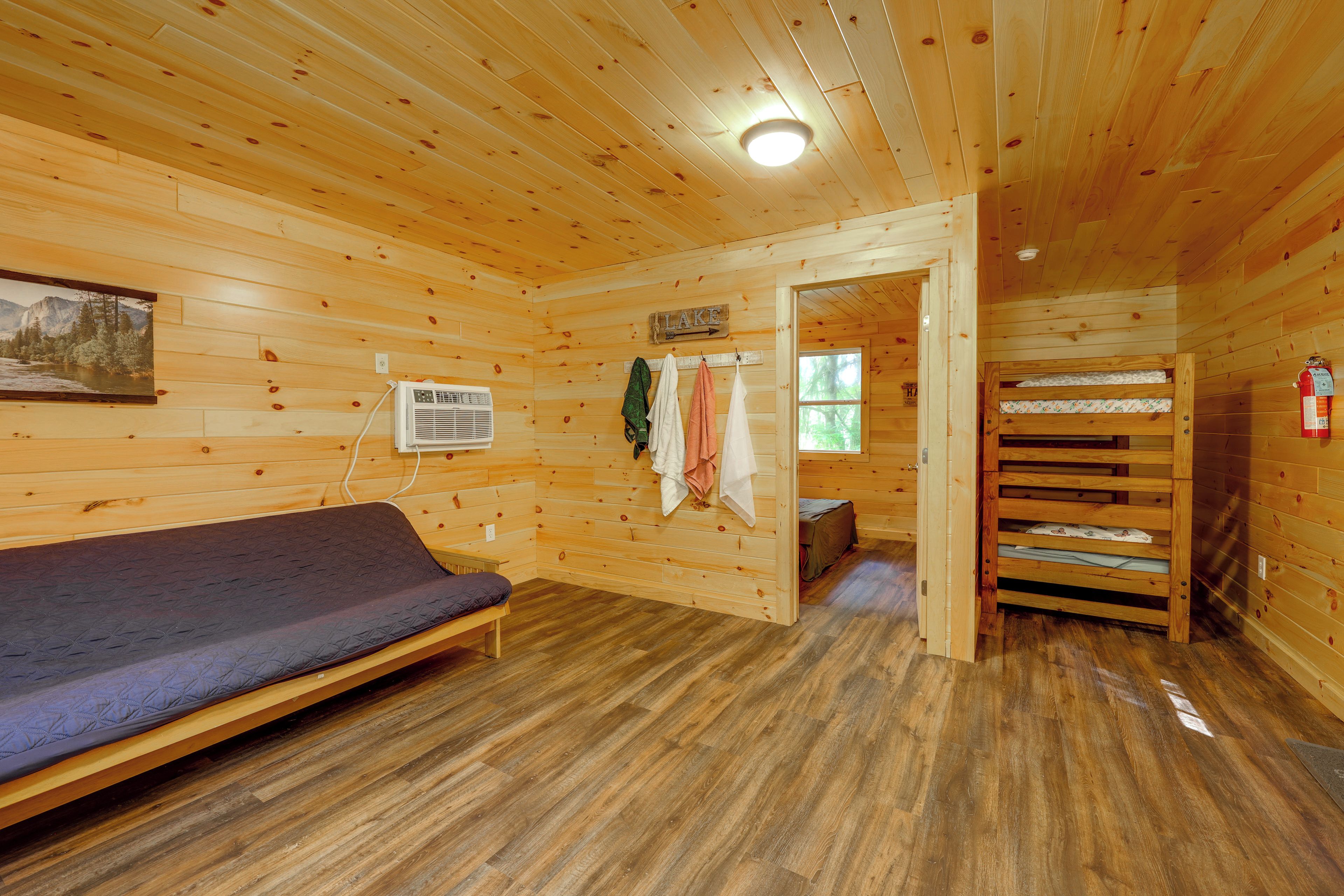 A cabin interior with a bed, a wall-mounted heater, and a door leading to another room.