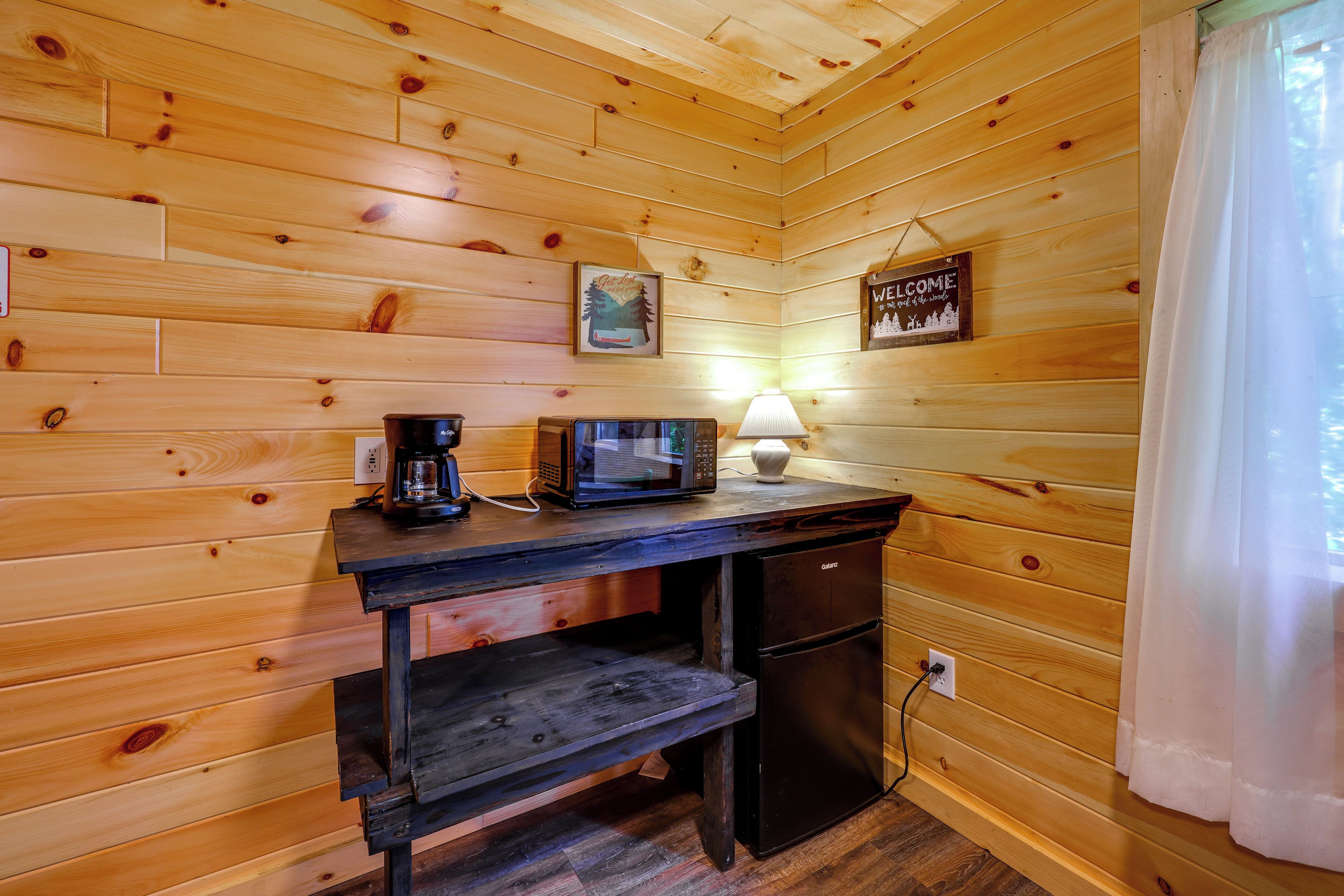 A wooden cabin interior with a kitchenette, a coffee maker, a microwave, and a small refrigerator.