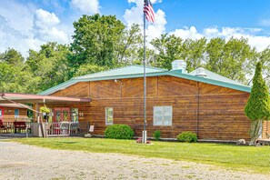 A rustic wooden cabin with a green roof, a flagpole with an American flag, and a small porch with outdoor seating. - Fun-filled Getaway at Letchworth Valley Resort (Bliss)