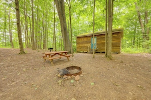 Una cabaña rústica con mesa de picnic y fogón en un área boscosa.