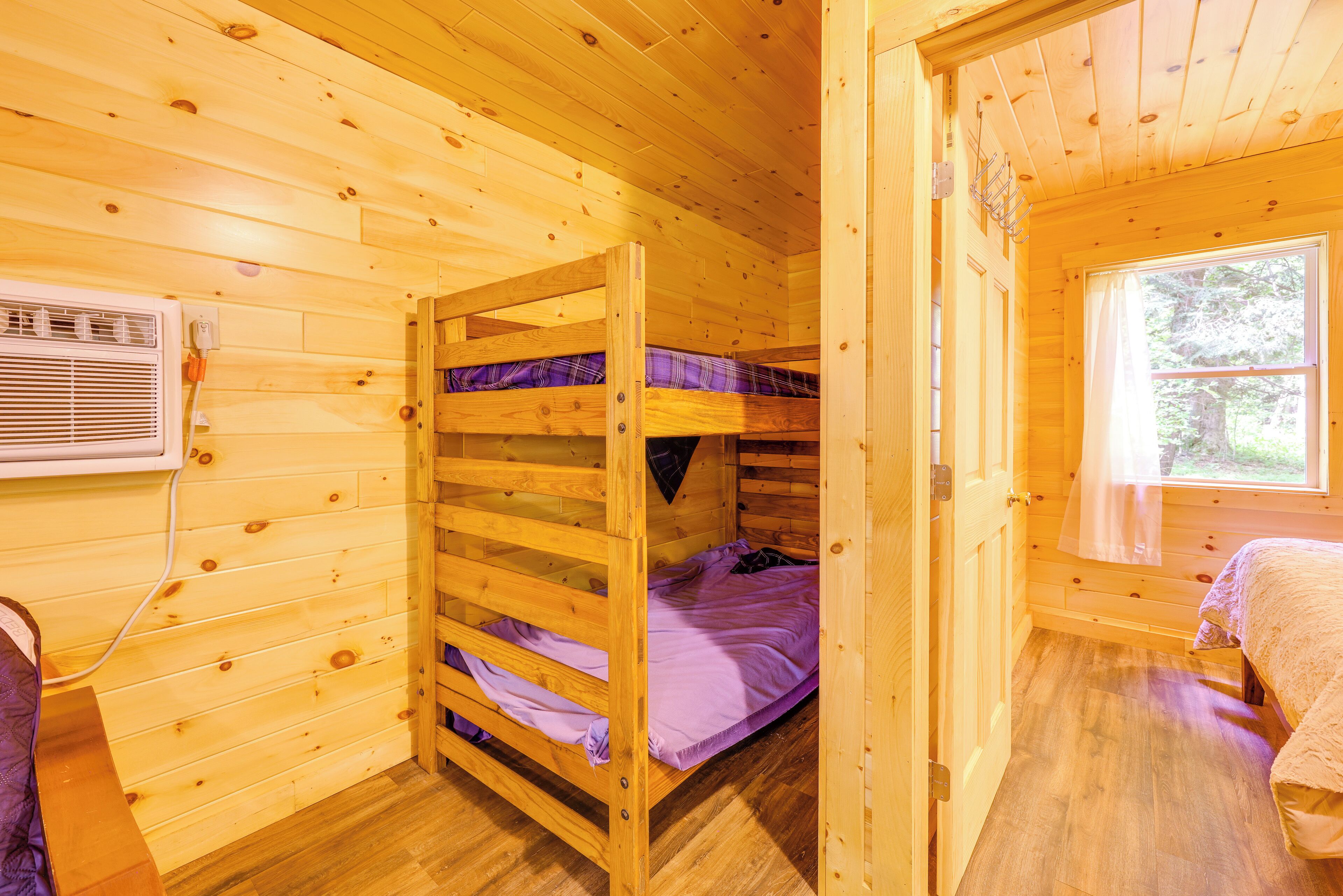 A wooden cabin room with bunk beds, a window, and a wall-mounted heater.