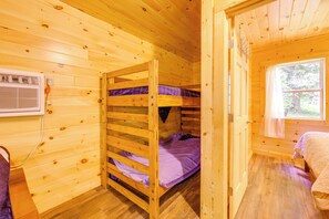 A wooden cabin room with bunk beds, a window, and a wall-mounted heater.